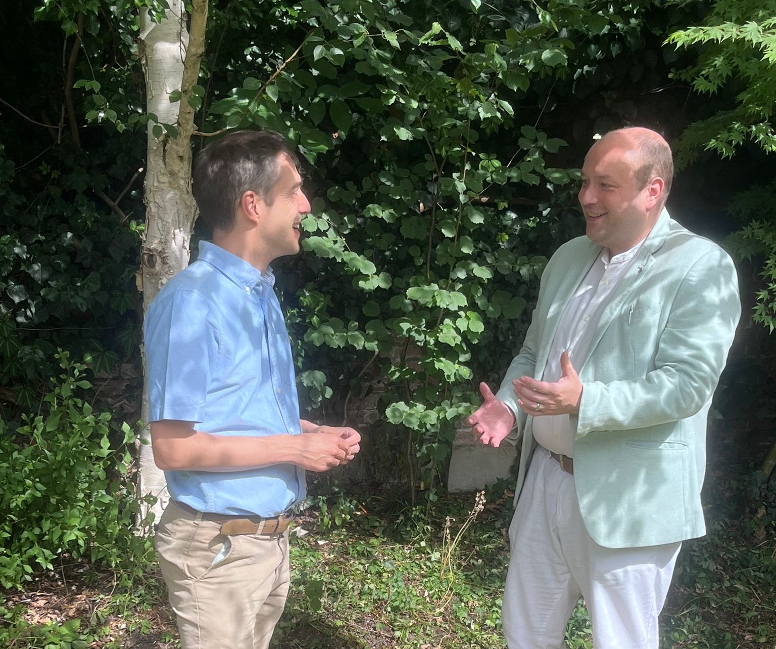 two people speaking to one another in front of hedge